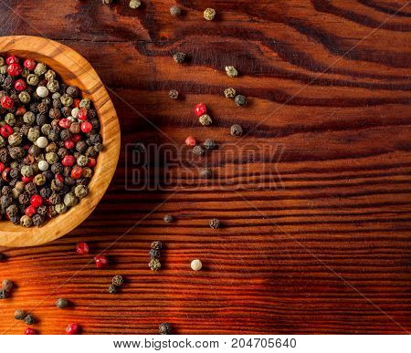 Peppercorns in a wooden bowl on a dark wooden background.