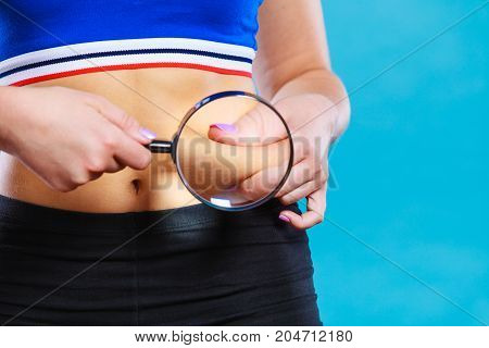 Woman pinches her waist examining it with magnifying glass. Fat lose liposuction and cellulite removal concept.