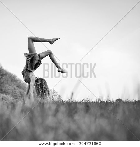 Young woman with flexible body doing somersault on spring green grass