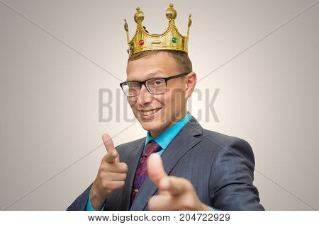 Winner. Award ceremony. First place man. Top manager. Young successful business man in suit and glasses with golden crown on his head showing success symbol. Vip client. Premium user. Success.