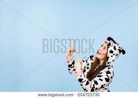 Happy teenage girl in funny nightclothes pajamas cartoon style pointing up with positive surprised face expression studio shot on blue. Advertisement concept