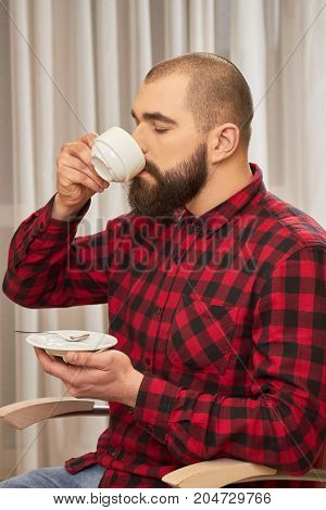Bearded man drinking coffee. Caucasian male holding white cup. The taste of manliness.
