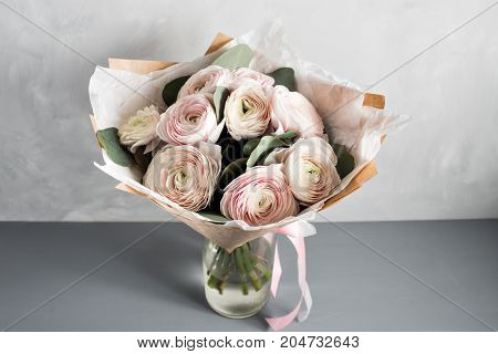 Little delicate elegant bouquet of flowers, buttercups and eucalyptus in tin can and a teacup on white gray table, morning breakfast.