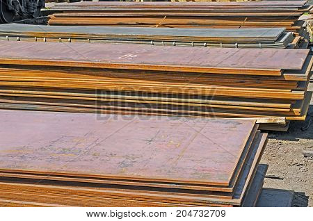 The rusty hot-rolled sheet metal in packs at the warehouse of metal products piled in the open air