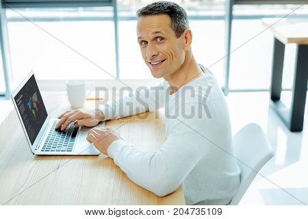 True workaholic. Positive smart handsome man being in his office and concentrating on work while doing his job