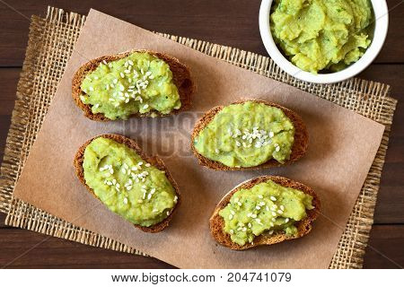 Toasted bread slices with green pea and parsley spread garnished with white sesame seeds photographed overhead with natural light (Selective Focus Focus on the top of the spread on the breads)