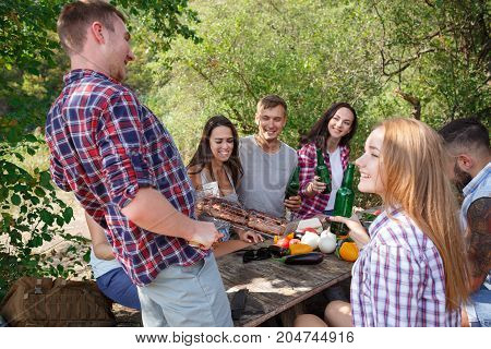 Romantic picnic. Group adult friends enjoying a healthy outdoor meal sitting together at a table in a lush green garden laughing and joking. Friends Outdoors Nature Picnic Chilling Out Unity Concept.
