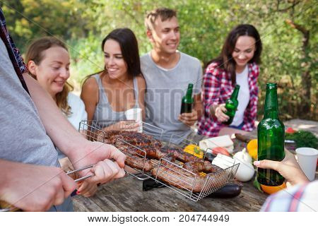 Romantic picnic. Group adult friends enjoying a healthy outdoor meal sitting together at a table in a lush green garden laughing and joking. Friends Outdoors Nature Picnic Chilling Out Unity Concept.