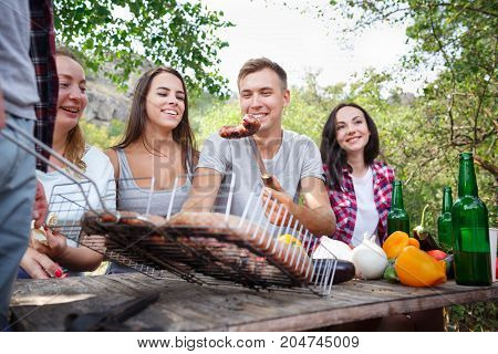 Romantic picnic. Group adult friends enjoying a healthy outdoor meal sitting together at a table in a lush green garden laughing and joking. Friends Outdoors Nature Picnic Chilling Out Unity Concept.