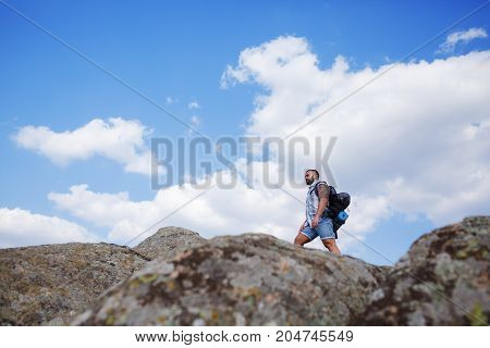 The guy looks into the distance, standing on the mountain. Beautiful mountain view on the background. Man in search of a way. Summer trip through the mountains without a map. Summer time.