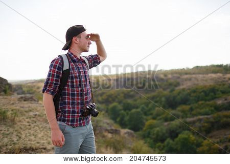 The guy looks into the distance, standing on the mountain. Beautiful mountain view on the background. Man in search of a way. Summer trip through the mountains without a map. Summer time.