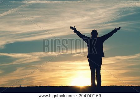 a woman at sunset with her arms raised in joy.