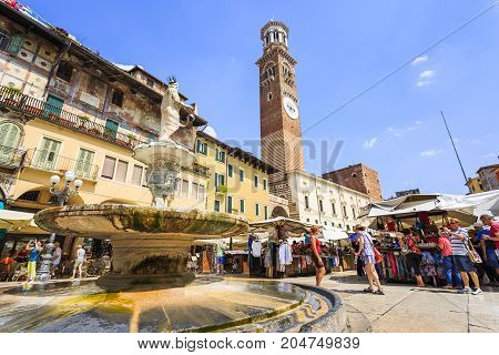 VERONA ITALY - JUNE 25 2016: Horizontal wide picture of the Piazza delle Erbe with the Fontanna Madonna Verona Torre dei Lamberti and tourists in a sunny day with clouds. Verona Italy.