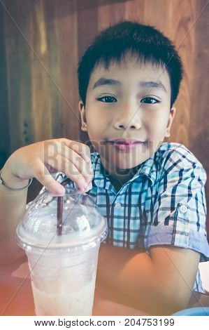 Handsome asian child smiling and looking at camera with cool milk after his lunch at restaurant with bright sunlight. Closeup happy boy enjoy eating. Vintage effect tone.