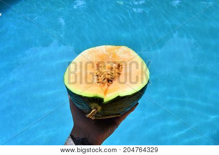 melon in the hand over the pool. juicy melon. summer day. fruits pool. fruits and sea. vacation time. swimming pool. swimming pool food. healthy fruit. spa vacation. travel concept. relax time.