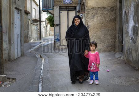 Fars Province Shiraz Iran - 18 april 2017: Smiling Muslim woman in Khimar standing in the yard and holding the hand of a little girl in a pink dress.