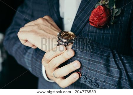 Cropped shot of a groom wearing elegant blue checked suit with rose butonniere and a wrist watch.