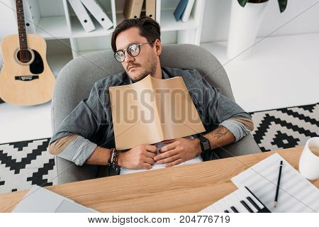 exhausted young musician sleeping with magazine at workplace