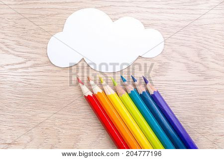 Paper cloud and rainbow rain from Seven pencils of rainbow colors lie on wooden table. Copyspace. Back to school. Wooden background.