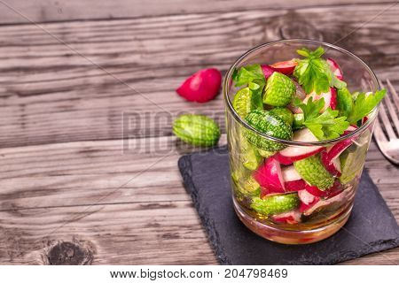 Glass of cucamelon and radish salad on wooden table with copy space