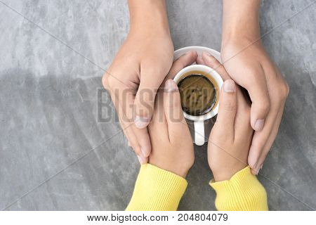Top view of close-up young couple is holding hands and coffee cup on the table.