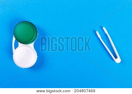 Tweezers with contact lens and plastic container on nlue background.