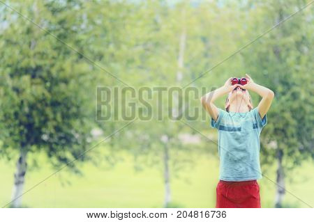 boy looks up through binoculars. the child throws back his head and watches something in the sky. The concept of surveillance. blurred background. Copy space for your text