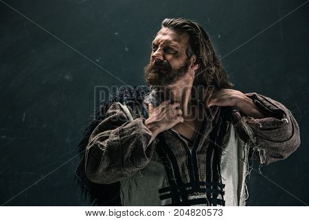 Actor in makeup, a poor man on black studio background. The bum in canvas rags. concept of vagrancy and survival. concept of pain and suffering