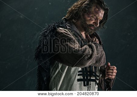 Actor in makeup, a poor man on black studio background. The bum in canvas rags. concept of vagrancy and survival. concept of pain and suffering