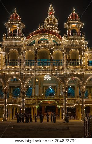 Mysore India - October 27 2013: Frontal shot of East facade center of Mysore Palace at nightly Sound and Light show. Beige building with towers and maroon domes. Central tower with golden domes. Music band.