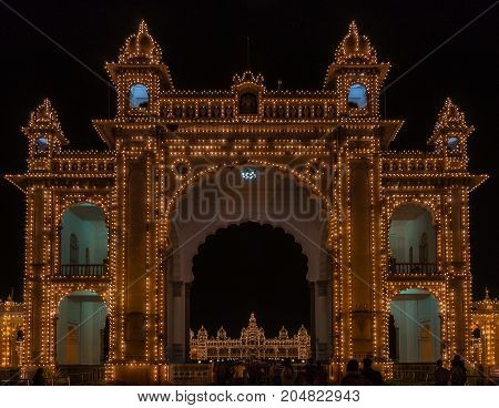 Mysore India - October 27 2013: Main East gate of Mysore Palace illuminated at nightly Sound and Light show. Palace self visible through gate. Hundreds of lights. Seen from outside domain.