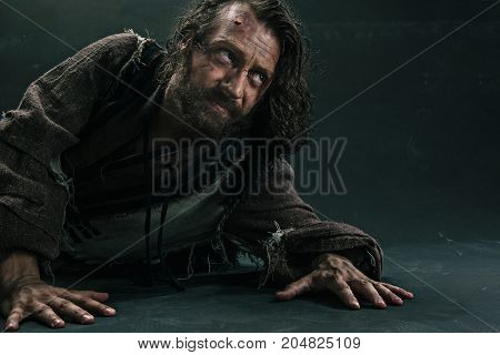 Actor in makeup, a poor man on black studio background. The bum in canvas rags. Concept of vagrancy and survival. Concept of pain and suffering. The wounded man crawling to salvation
