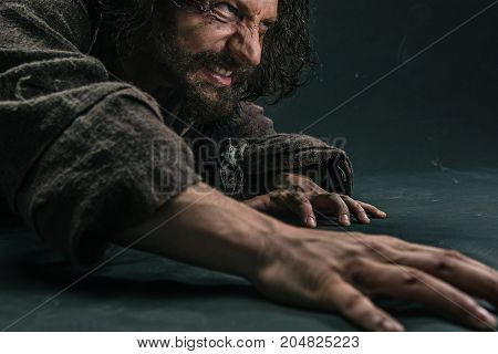 Actor in makeup, a poor man on black studio background. The bum in canvas rags. Concept of vagrancy and survival. Concept of pain and suffering. The wounded man crawling to salvation