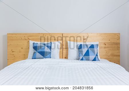 empty cozy white bed with blue and white pillows and wooden headboard in white bedroom good for minimalist or young and modern lifestyle concept