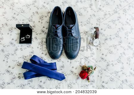 Groom's shoes and cufflinks, blue tie, wristwatch, boutonniere on a light background. Wedding concept. Artwork, soft focus
