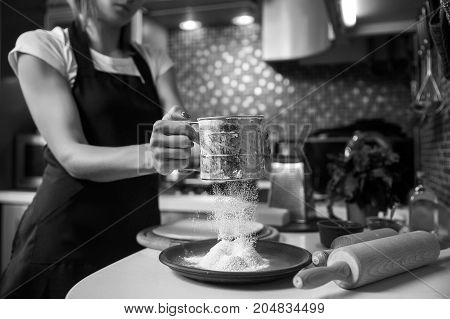 Woman sifting flour through sieve In the kitchen. Selective focus.
