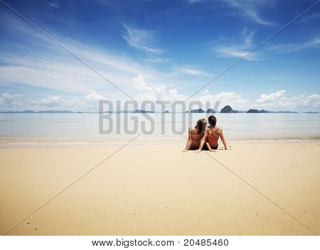 Ung familie sidder på varmt sand af et hav og leder til et sted