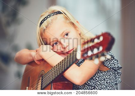Tired little girl learning to play to the guitar at the home.
