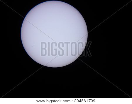 the sun viewed through a solar filter in a telescope with sunspot visible
