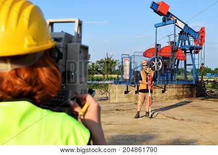 Two surveyors at work on an eastern Europe oil well with crude oil pumpjack in background