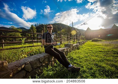 Young man works at laptop outdoor in the mountains at sunset