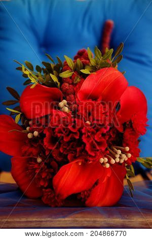 Wedding decoration. Bridal bouquet made of beautiful red flowers placed at the chair with blue cushion.