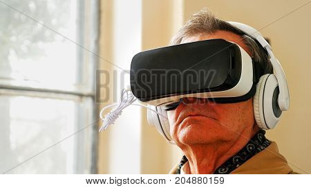Senior old man wearing VR headset and enjoying virtual reality digital world. Virtual and augmented reality are increasingly used in human lives.