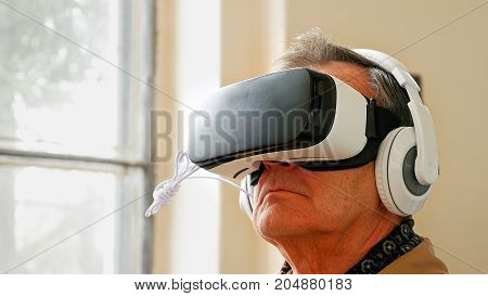 Senior old man wearing VR headset and enjoying virtual reality digital world. Virtual and augmented reality are increasingly used in human lives.