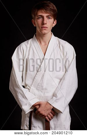 Portrait of a young student wearing white kimono with a belt on a black background. Gorgeous student learning eastern fighting techniques.