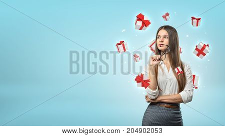 A young businesswoman stands thinking while small white and red gift boxes fly around her head. Ideas for presents. Choose client bonuses. Free gifts selection.