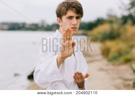 Young professional karate fighter in a blocking position. Boy on a jui-jitsu training on a blurred natural background.