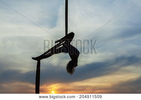 Woman's equilibrist does tricks high in the sky in the setting sun. Only the contours of the athlete.