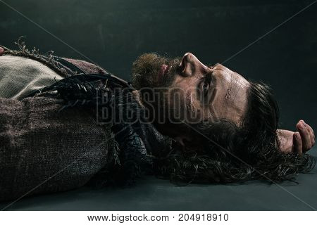Halloween zombie lying on paving asphalt. Vampire hipster with red blood outdoors. Holiday celebration concept. Man with bloody beard and hair. War soldier with wounds on face.
