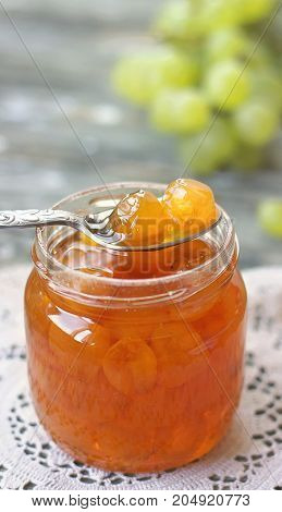 Slatko - preserved white grapes on silver spoon in glass jar on wooden background; traditional serbian desert of white grapes or white cherries